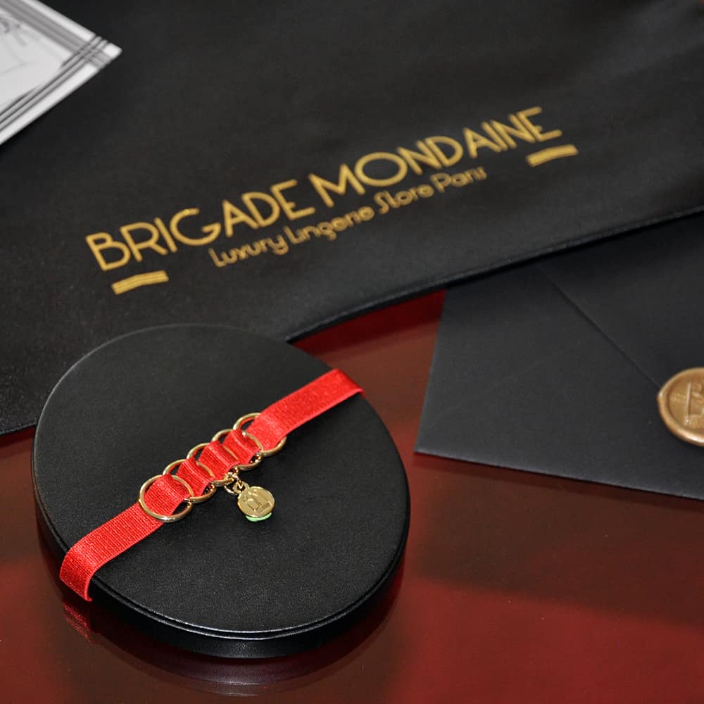Hier sehen Sie das Luxus-Geschenkpaket der Marke Brigade Mondaine. Darin befindet sich ein roter Chocker mit seinem Beutel und einer signierten und gewidmeten Karte nur für Sie. All dies ist in einem schwarzen Seidenbeutel enthalten.