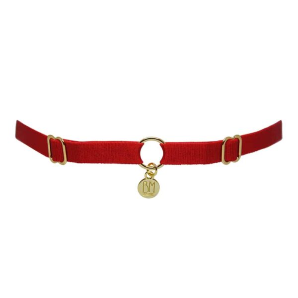 Ici vous pouvez voir le BRIGADE MONDAINE GIFT WRAP RED. Ce collier est fait d’une bande rouge. 2 détails pour régler les bandes se trouvent à droite et à gauche. Au milieu, la bande est séparée par un anneau plaqué or avec un pendentif où il est inscrit « BM ».