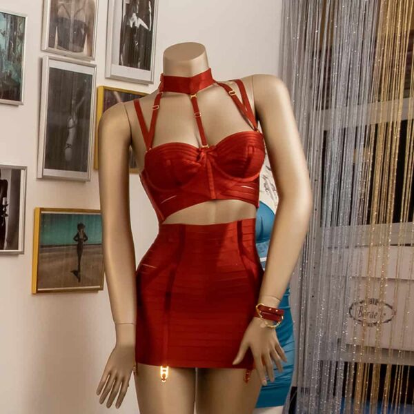 The model is wearing a Signature Bordelle set in red. It is composed of a Minerva Ruby bustier and an Exclusive Classic Waspie Ruby, both made of red satin and fishnet elastic and gold plating.
