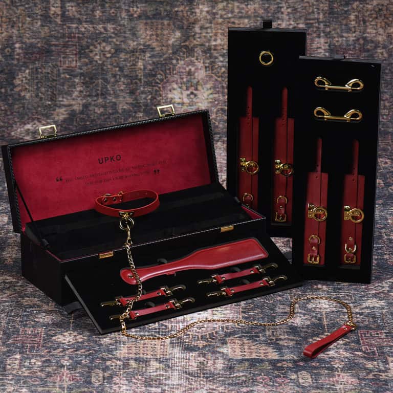 Red leather bondage and BDSM accessory trunk including collar, leash, handcuffs and spanking paddle