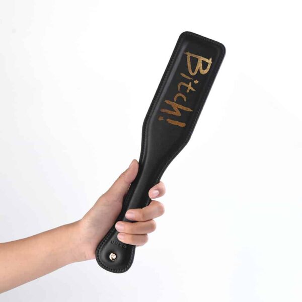 Spanking paddle in black leather and gold finish with gold inscription UPKO at Brigade Mondaine