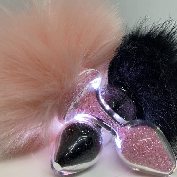 Imagen de dos tapones superpuestos, uno rosa y otro negro, llenos de cuentas brillantes de sus respectivos colores, cada uno adornado con una cola de conejo suspendida.