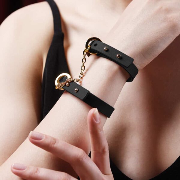 Thin black leather bracelet with 24K gold handcuff attachment at Brigade Mondaine