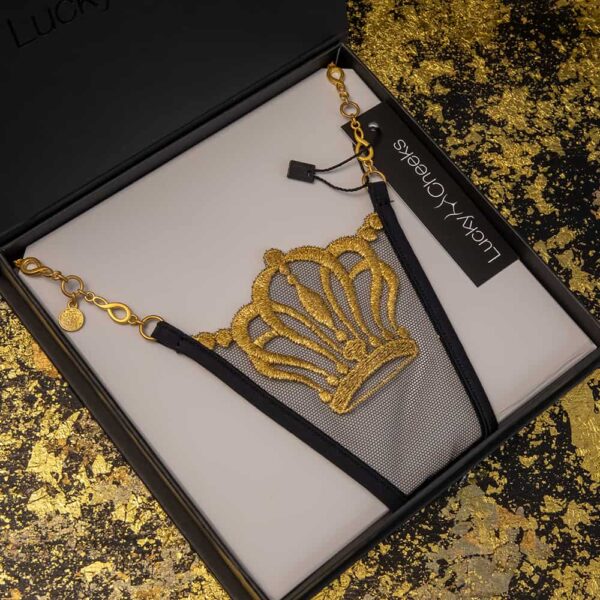 Lucky Cheeks String in schwarz und gold, mit Schweizer Stickerei, die eine Krone darstellt, und einer Schmuckkette aus goldfarbenem Zamak.