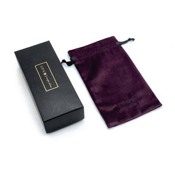 Black box with decorations and golden logo of the UPKO brand with its burgundy velvet pouch to store the limited edition handcuffs of the UPKO X Brigade Mondaine collaboration presented on a white background at Brigade Mondaine