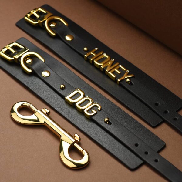 Pair of handcuffs in soft black Italian leather laid flat with the words DOG and HONEY in 24 carat gold-plated letters with stone inlaid on each letter all laid flat on a brown background with a light coming from the top left corner of the l'image being ideas for the handcuffs of the UPKO X Brigade Mondaine collaboration