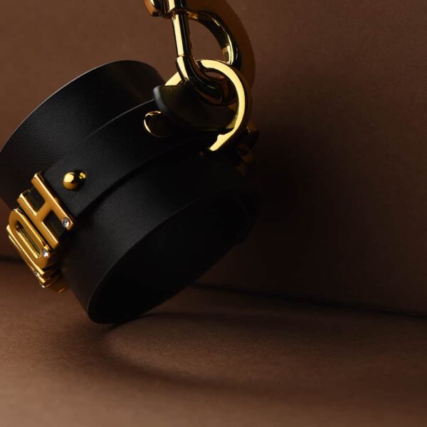 Close-up view of d'an Italian black leather handcuff with 24 carat gold-plated and engraved by the brand UPKO for l'limited edition UPKO X Brigade Mondaine at Brigade Mondaine