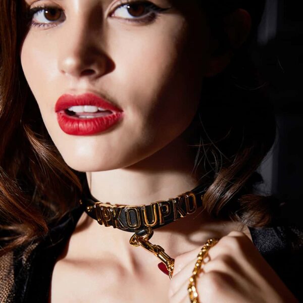 Necklace with UPKOUPKO markings in gold lettering and 24 carat gold-plated ring worn around the neck d'a mannequin and in close-up view attached to a leash that d'inspiration for the products of the collaboration UPKO X Brigade Mondaine
