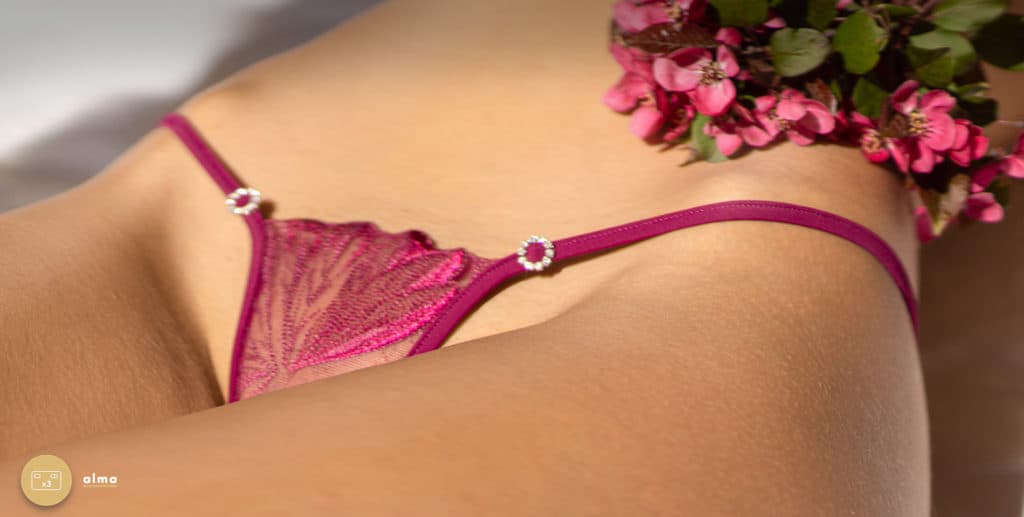 Das Model trägt einen String der Marke Lucky Cheeks. Set String Juwel Purple Temptation, violetter String aus transparenter Spitze mit einer Schnur, die mit zwei Ringen aus Swarovski-Strass verziert ist.