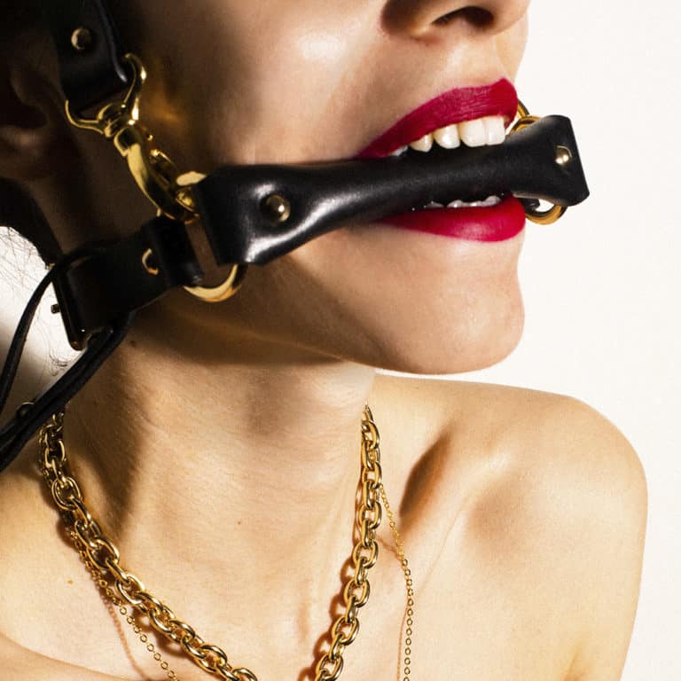 Gag head harness in black leather from Elif Domanic. A strap placed at the level of the mouth is maintained by two golden rings to another strap which is placed at the back of the skull. Another strap much longer is attached to the whole by a loop and loops.