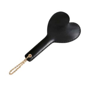 Spanking paddle from the brand Elif Domanic. The product has a straight black leather handle with a gold eyelet and chain on the left end, the right end has a black leather heart shape. The whole is stitched with a black seam.