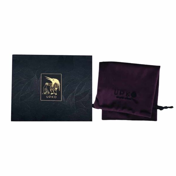 Die Verpackung des UPKO-Bondagegürtels besteht aus einer purpurfarbenen Samttasche mit dem schwarzen UPKO-Schriftzug. Die Schachtel besteht aus einem schwarz-silbernen Blattwerkboden mit einem zentralen Quadrat, das den Schriftzug und das Logo der Marke UPKO in goldener Farbe zeigt.
