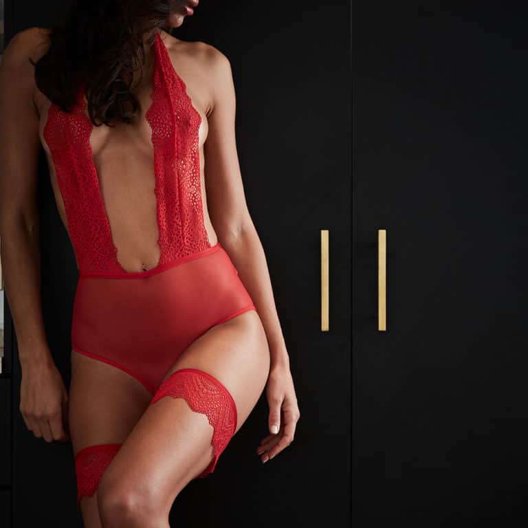 Body Ouvert Rouge Atelier amour de la collection Nommée Désir. Ce body comporte deux larges bandes de dentelles placés de la nuque au nombril en laissant entrevoir la poitrine. La dentelle fine laisse la silhouette tout en transparence. Un tour de taille élastiqué sépare le bas du body qui est une pièce de tulle en transparence. Le dos est complètement dénudé, il n’y a que la partie du fessier qui est couverte de tulle et de dentelle entrouverte. Des réglettes dorées à la nuque et à la taille permettent d’ajuster la taille du body. Au niveau de l’entrejambe une ouverture laisse entrevoir les parties intimes pour un peu plus de sensualité.