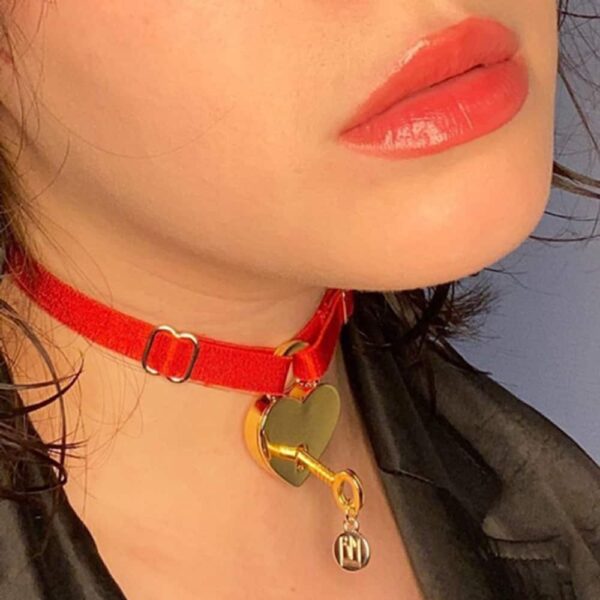 Choker rouge de la Brigade Mondaine aux finitions doré de 24 carats , anneau au milieu avec une attache pendante écrit BM. Acammpagné de cadenas à coeur