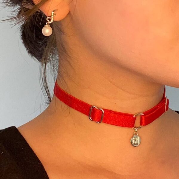 BM necklace included in the Brigade Mondaine gift pack. The product is a simple choker with a red elastic necklace and a gold pendant embossed with the Brigade Mondaine logo. This jewelry is attached to the necklace by a ring. The whole product is adjustable.