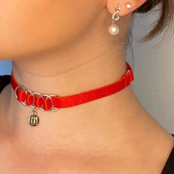 Collier BM inclut dans le pack cadeau Brigade Mondaine. Le produit est un choker simple avec un tour de cou en élastique rouge et un pendentif doré embossé du logo Brigade Mondaine. Ce bijoux est attaché au collier par quatre anneaux soutenus par l’entrelacement de l’élastique. L’ensemble du produit est réglable.