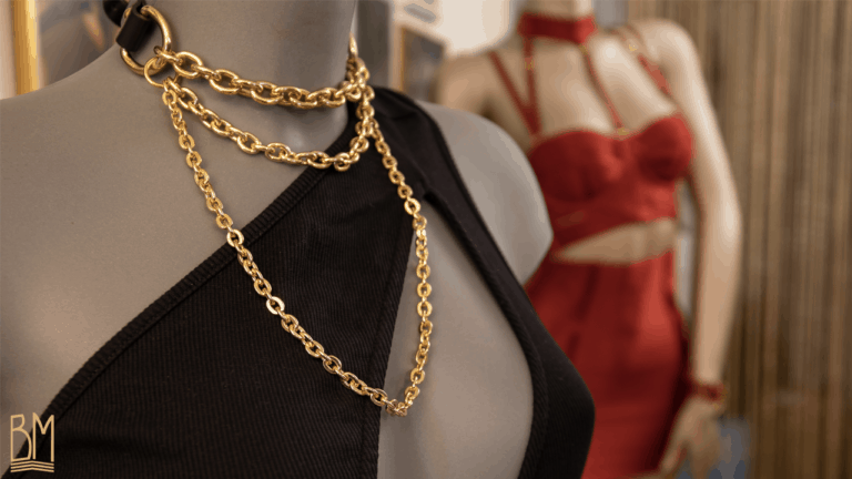 Nous pouvons voir un mannequin portant portant un chocker bondage Elif Domanic en couleur or. Il possède des chaîne or ainsi qu’une attache en cuir noir sur la nuque.