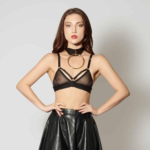 Leather Artefact Chocker O Noir de la marque ELF ZHOU LONDON. Le chocker est cuir noir et possède au centre de celui-ci une grosse boucle en or. Le modèle porte un soutien triangle noir transparent ainsi qu’une jupe noir en cuir. Elle se tient debout, les bras sur les hanches et regarde l’objectif.