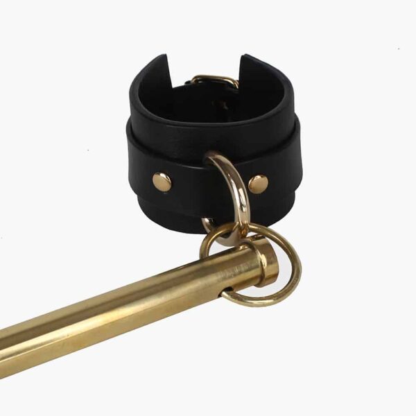 Spreader bar of the brand Elif Domanic. Two handcuffs with a gold colored buckle support a long and thin bar by two rings