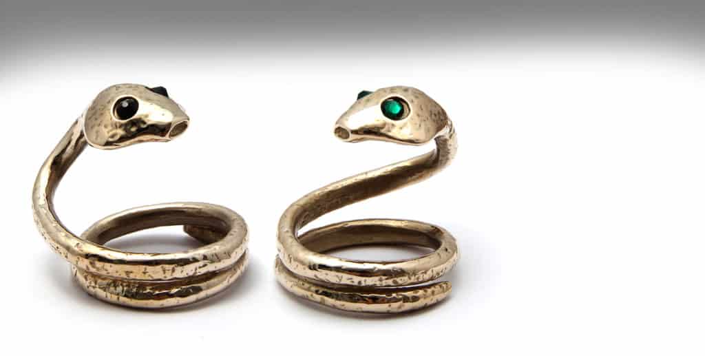 Hier sehen Sie zwei Eichelhelme der Marke ROSEBUDS in Form einer Schlange. Der Kopf der Schlange verfügt über zwei Augen. Die Augen werden durch Edelsteine von Swarovski dargestellt. Einer hat grüne Augen und der andere schwarze Augen. Der Schwanz des Schwurs