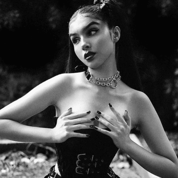 Black and white photograph of a woman wearing a black corset and a chain necklace with a gold and leather ring.