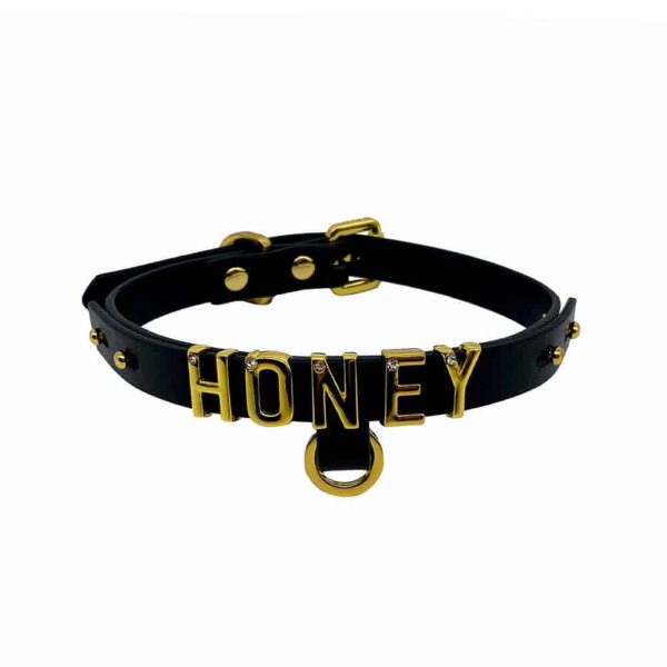 Collar / gargantilla de suave cuero italiano negro con gancho y letras bañadas en oro de 24 quilates y una pequeña piedra incrustada en cada letra que escribe la palabra HONEY de la colección UPKO X Brigade Mondaine disponible en Brigade Mondaine