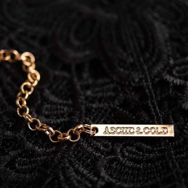 Halskette Alodie der Marke ASCHE & GOLD in Goldfarbe. Sie ist aus Leder gefertigt und mit drei gunfarbenen Ringen verziert, die sich als zentraler Schmuck ineinander verschlingen.