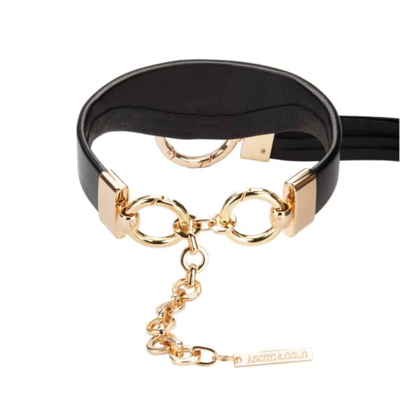 Ava Schwarze Lederhalskette der Marke Asche&Gold, erhältlich bei Brigade Mondaine. Die Halskette ist dick und aus Leder mit ihren goldenen Beschlägen. Vorne gibt es einen langen schwarzen Lederfranchise, der an einer goldenen Schnalle hängt.