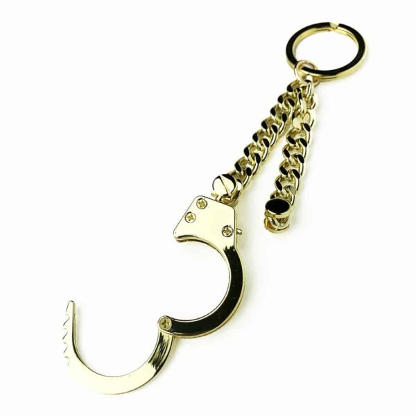 Leather keychain handcuffs of the brand ELF ZHOU LONDON. The keychain contains a gold chain at the end of which is open handcuffs.