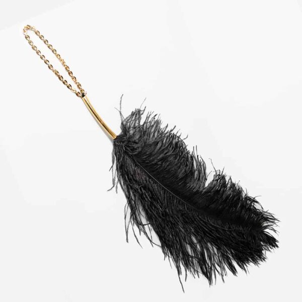 Teaser pluma de avestruz de Elif domanic. La pluma es de color negro. En el extremo de la pluma hay una fina asa circular de oro y en el extremo un largo lazo de cuentas de oro.