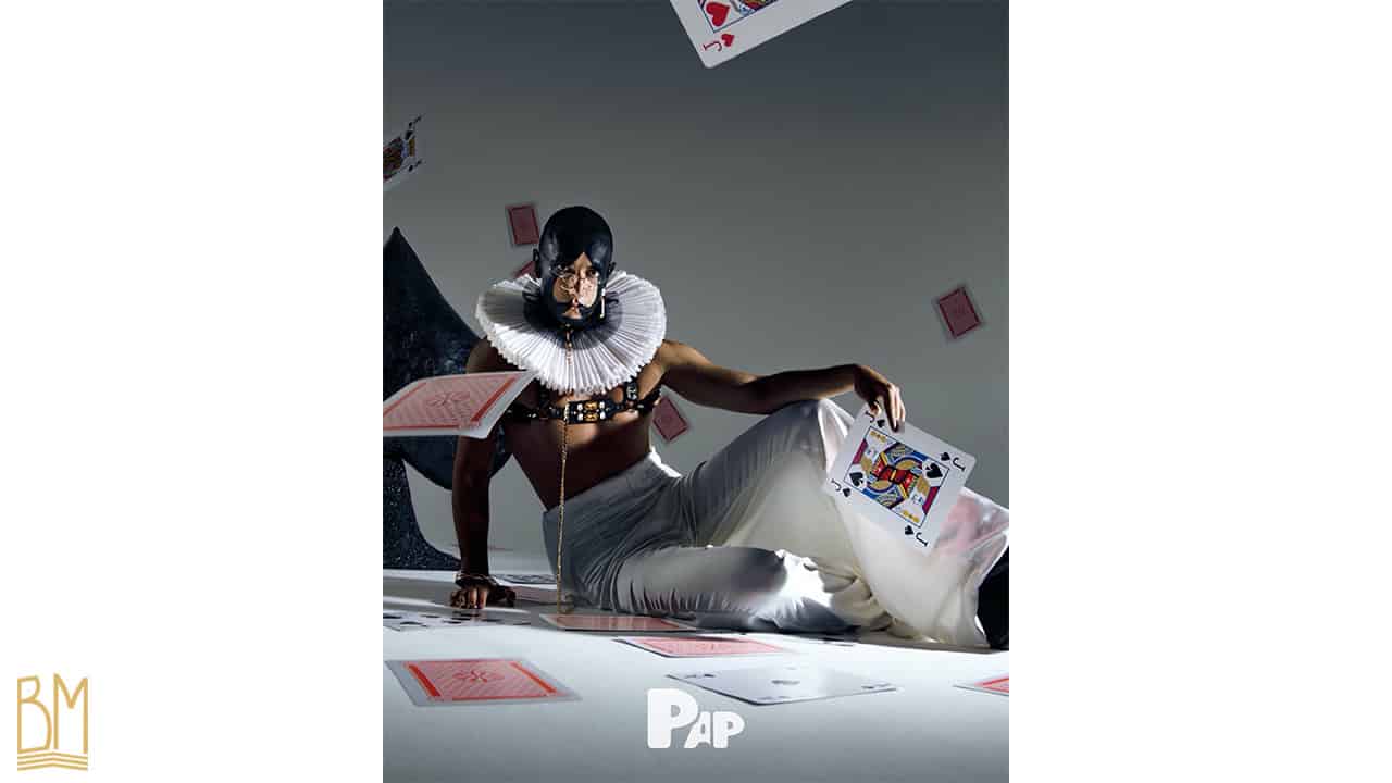 PAP Magazine es handelt sich um einen Mann, der eine Leine der Marke Upko trägt. Sein Gesicht ist schwarz bemalt und bildet das Zeichen für Pik. In seiner Hand hält er eine Pik-Bube-Karte. Hinter ihm fallen Karten herunter und weitere Karten sind auf dem Boden verstreut.