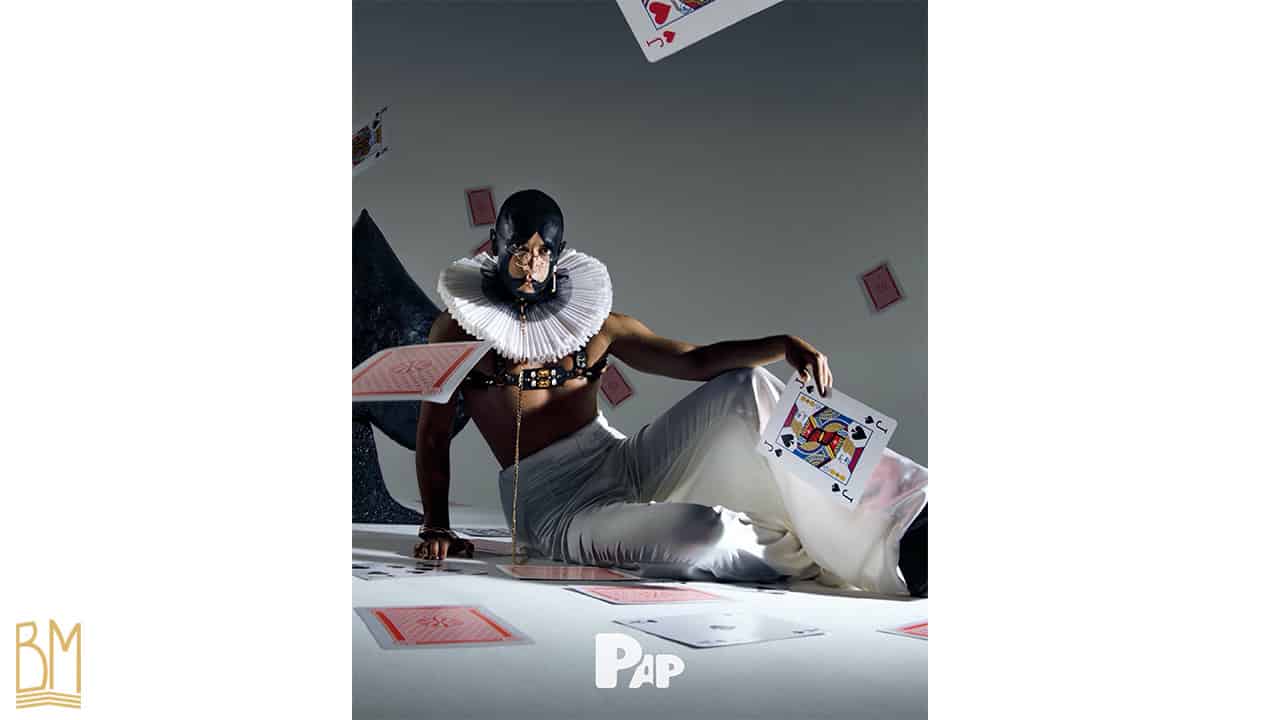 PAP Magazine it is a man wearing a leash of the brand Upko. His face is painted in black and forms the sign of the spade. He is holding a jack of spades card in his hand. Cards fall behind him and other cards are scattered on the ground.