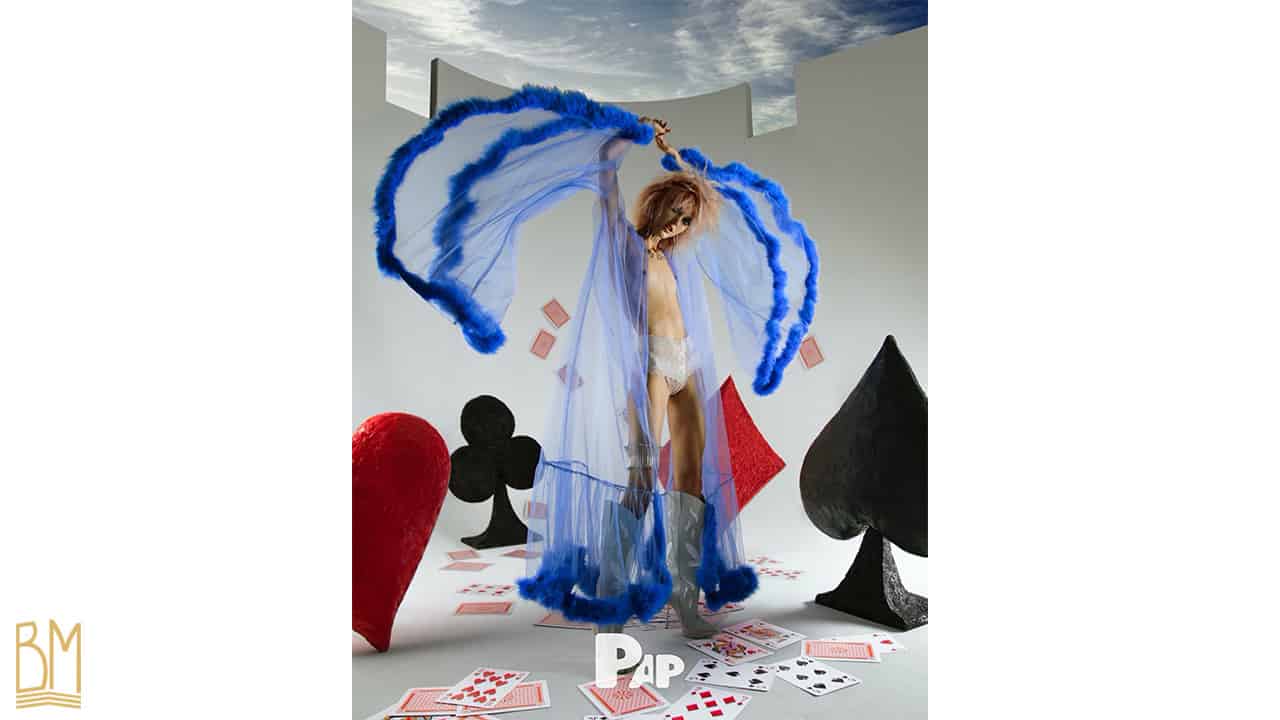 PAP Magazine Il s’agit d’une femme portant . Par dessus elle porte une culotte G-string de la marque Bracli. Derrière elle, se trouve le signe du coeur, du trèfle, du pique et du carreau. On peut voir sur le sol des cartes éparpillés et d’autres qui tombent.
