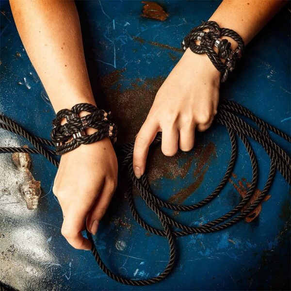 Schwarze Armbänder aus langem schwarzem Seil mit Metallbeschlägen. Armbänder, die zu vier Schlaufen mit Metallbefestigungen in der Mitte geknüpft sind.