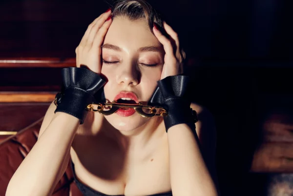 Woman in black leather handcuffs with gold links entering her open mouth