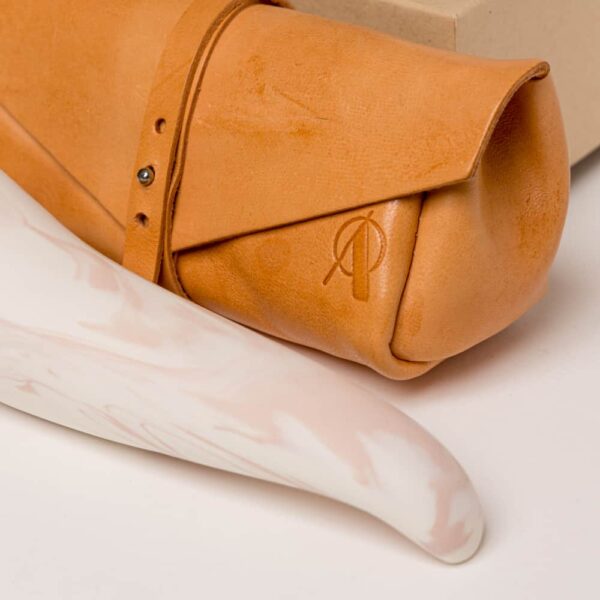 Orange leather pouch with the brand's logo on it. The thick spur on the top and thinner tip, it is porcelain colored pink and white from Adeles Brydges at brigade mondaine