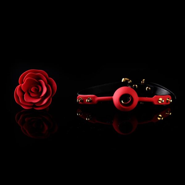 Pink Ball Gag from the brand Upko x Zalo. The product is detached, the back of the product is black and the front is red. The center of the Ball Gag is shaped like a red rose. The whole is placed on a black background.