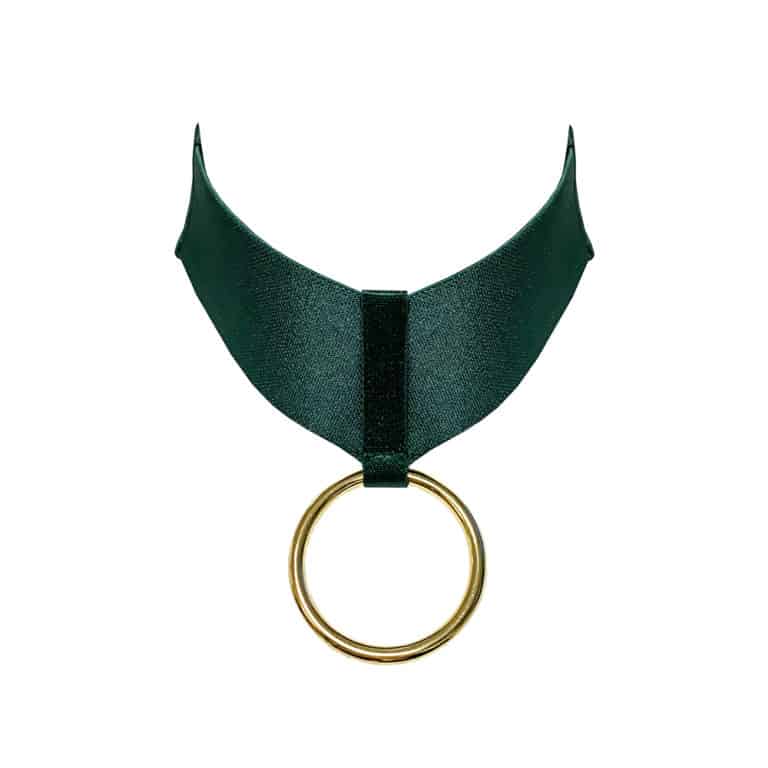 Бондажное ожерелье из коллекции Kora от Bordelle. Это ожерелье цвета эдемской зелени. Он состоит из широкой эластичной ленты, в центре которой находится кольцо-подвеска, покрытое 24-каратным золотом. Кольцо удерживается на месте более тонкой резинкой в сочетании с широкой резинкой.