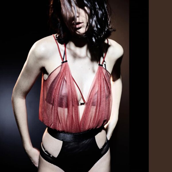 Bodysuit Incense Collection Caravasar of the brand Gonzales Affaires. This bodysuit is composed of two colors. First of all red that covers the chest to the waist. This part of the product is made of transparent tulle and is worked in the form of a drape that covers the chest. A wide black elastic belt divides the product and reveals the fabric that covers the belly and intimate parts in the form of single panties. A double strap is connected to the bodysuit.