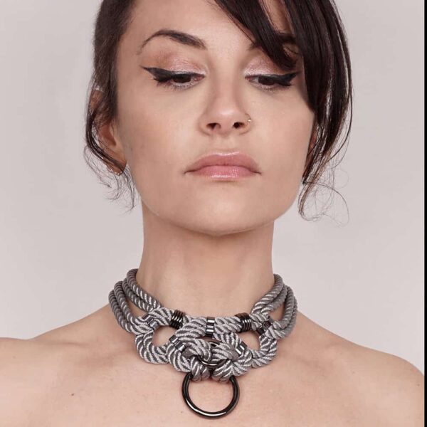 "Megami" means goddess in Japanese. This choker necklace will not leave anyone indifferent, both by its manufacture from waxed cotton rope and tied symmetrically, as well as by its design of intertwined knots with silver finishes. Closing on the neck. One size fits all & adjustable. This necklace is available at Brigade Mondaine.