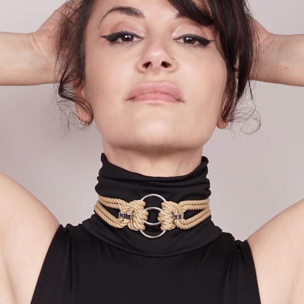 This elegant, snug-fitting choker features two O-rings intertwined with traditional symmetrical polyester rope knots. It is finished with silver zinc alloy and brass hardware. A satin ribbon can be tied in a knot in the back for a custom fit. One size fits all. It is available at Brigade Mondaine.