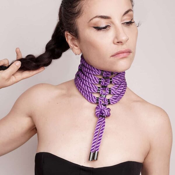 This Posture Collar wraps the neck following the curves of the body. It is snug but still comfortable and adjusts in the back with laces. It features a lover's bow in the center. The dangling rope tips are finished with zinc alloy metal caps. A stylish, high-impact piece. Back closure. Silver finish. Fully adjustable. One size fits all. This necklace is available at Brigade Mondaine.