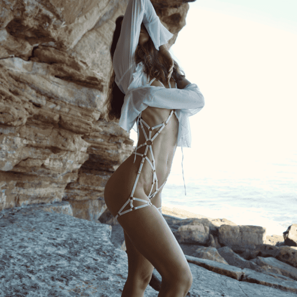 Photograph of a woman in front of rocks wearing a white harness with gold details and a white shirt.