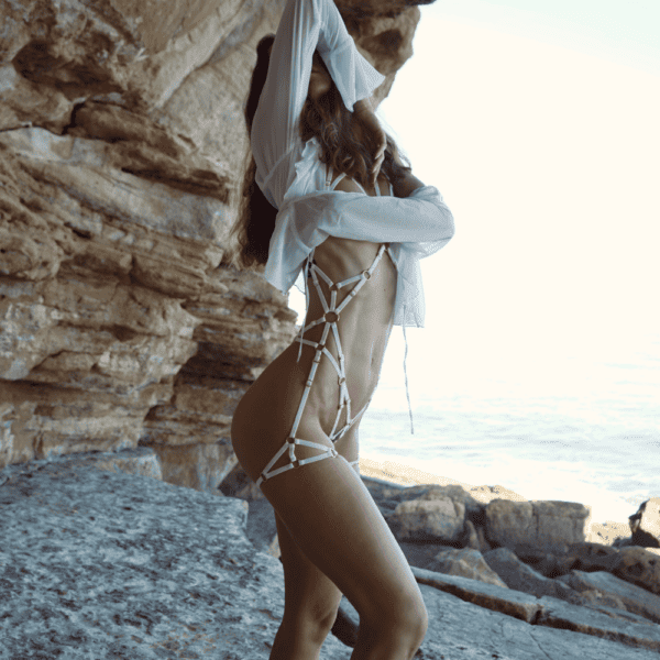 Photographie d'une femme devant des rochers portant un harnais blanc avec des détails dorés et une chemise blanche