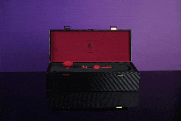 schwarzer Koffer mit rotem Innenleben. Darin befinden sich schwarze Upko-Accessoires und eine rote Ball-Gang-Rose.