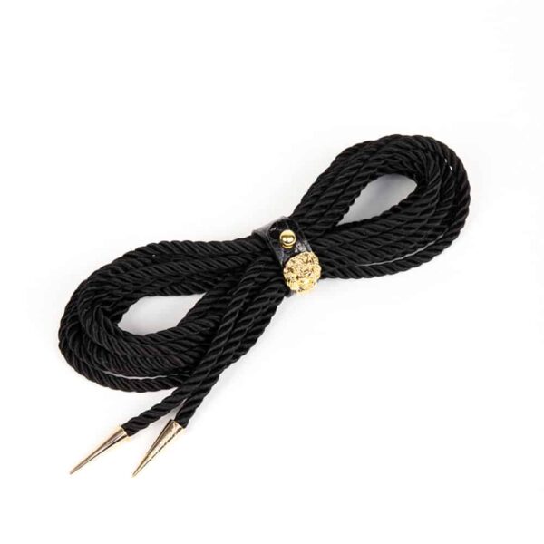 The Leone Lasso Shibari by Fraulein Kink. Bondage lassos have many versatile options for use inside or outside the bedroom. Wear it as a belt or harness to add a high fashion touch to your favorite outfit. 5 yards of black cord. Gold lion head tips. Secured with a croc-embossed leather strap with gold button.