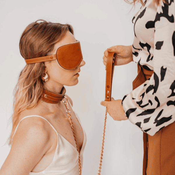 Photo of a woman wearing a mask, necklace and tan leather leash.