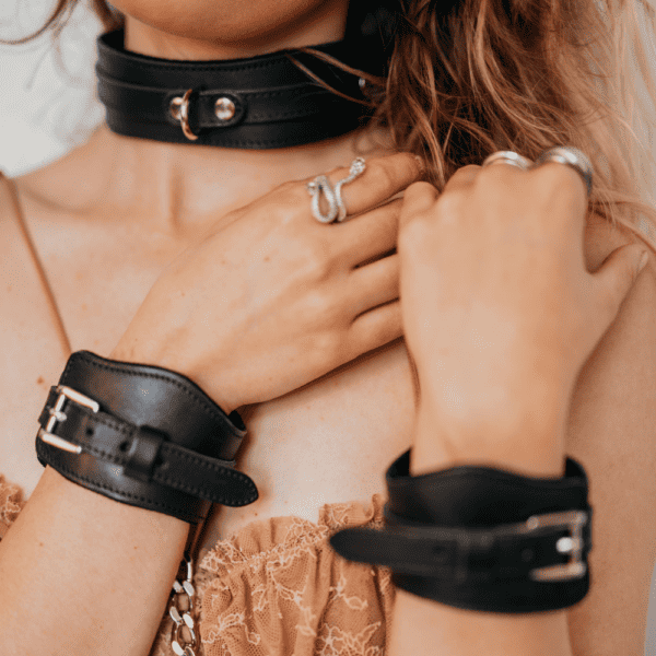 Photo of a woman wearing a black leather BDSM necklace and handcuffs.