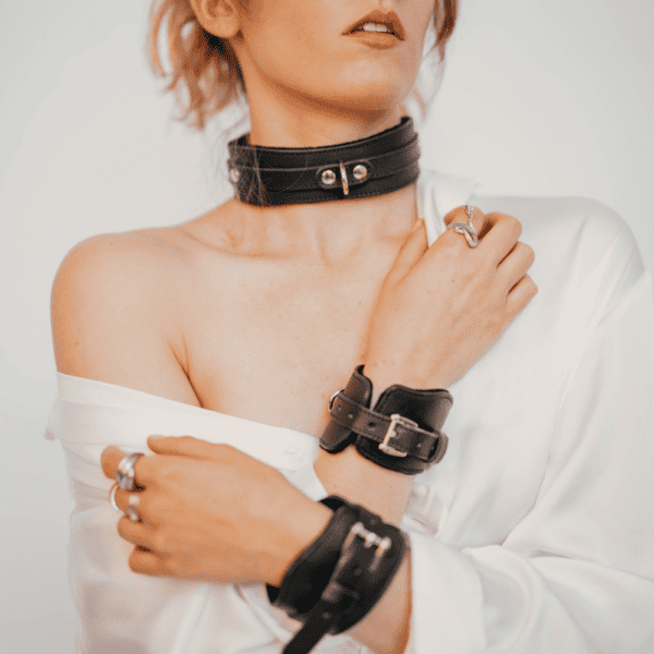 Photo of a woman wearing a black leather BDSM necklace and handcuffs.