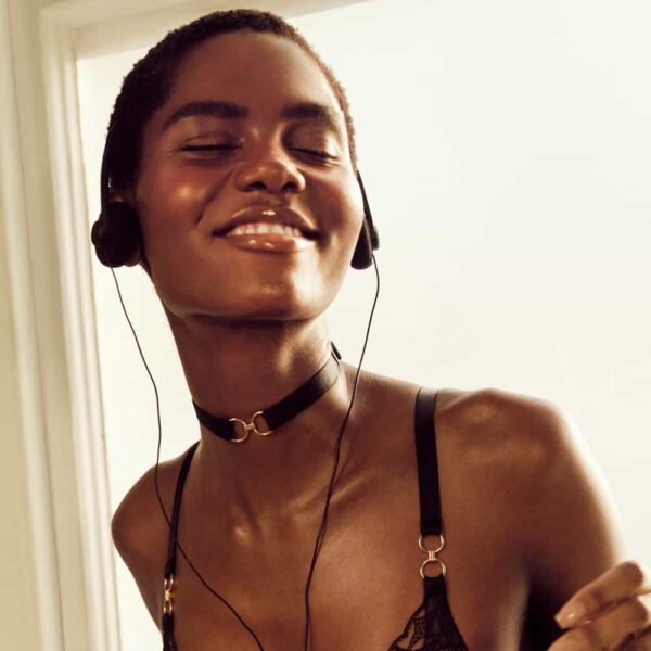 mujer sonriente escuchando musica en lenceria bordelle transparente detalles dorados rayas negras y cuello